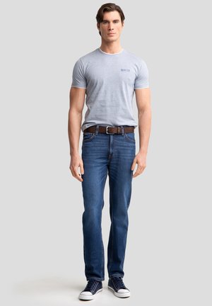 Light gray cotton t-shirt with short sleeves and blue logo, paired with dark blue denim jeans and navy high-top sneakers. Brown belt accent.