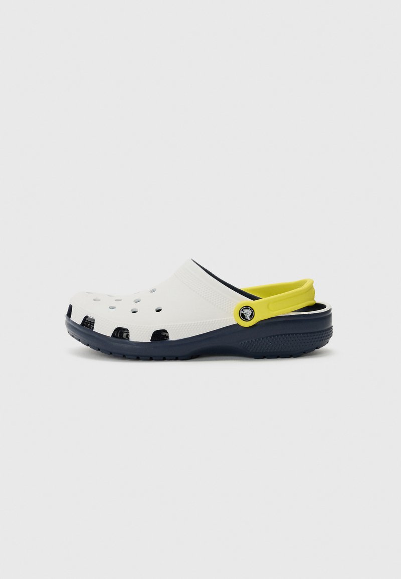 Tamanco branco com orifícios de drenagem pretos, detalhe amarelo na faixa do calcanhar e sola azul-marinho. Feito de material leve e durável.