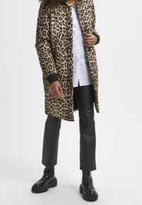Puffet jakke i leopardprint med sorte ribbede manchetter, båret over en hvid skjorte med knapper og parret med sorte faux læderbukser og kraftige sorte støvler.