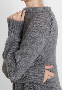 Maglione grigio lavorato a maglia con scollatura rotonda, polsini a costine e una texture morbida, che mette in risalto un design chunky e lavorato in modo rilassato.
