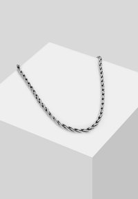 Sølv kædetræk med snoede led, glat overflade og et ensartet design, præsenteret mod en geometrisk grå baggrund.