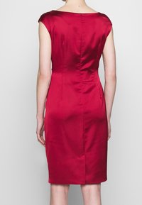Robe en satin rouge à la silhouette ajustée, manches courtes et fermeture éclair au dos. Texture lisse avec une légère brillance et design minimaliste.