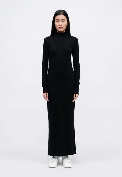 Melna garā piedurkne turtlenecka kleita, pieguļošs siluets, mīksta auduma, līdz potītēm ar pagarinātām piedurknēm, kombinēta ar baltām sporta apaviem.