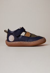 Chaussure en cuir marine avec semelle en caoutchouc beige, design découpé, bride réglable et patch logo sur le talon. Présente des détails cousus sur l'ensemble.