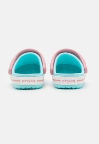 Two back view Crocs with a turquoise body and pink strap. Features a white stripe near the sole with "crocs" branding on the heel.