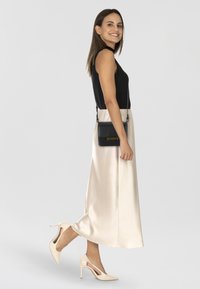 Top maniche corte nero a costine, gonna midi in raso crema, borsa a tracolla nera con dettaglio in oro e décolleté beige a tacco alto con dettagli ritagliati.