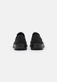 Chaussures de sport noires avec une tige en tissu lisse, un col rembourré et une semelle en caoutchouc texturé, conçues pour le confort et le soutien.