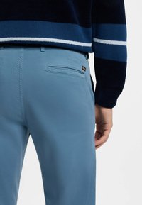 Světlé modré kalhoty s hladkým povrchem, se zadní kapsou a malou štítkovou nálepkou. Pas je upnutý, což doplňuje námořnický svetr.