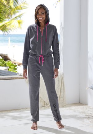 Gray hooded jumpsuit with a pink zipper and drawstring, featuring a logo on the left leg. Soft fabric and loose-fitting design.