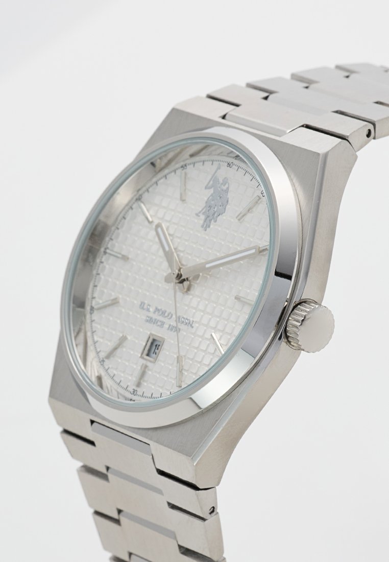Montre en acier inoxydable argenté avec un cadran blanc texturé, affichage de la date et logo. Elle possède un bracelet en métal brossé et des accents polis.