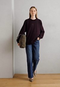 Sudadera negra de gran tamaño con logo, jeans de mezclilla anchos azules, zapatos de tacón alto plateados y un bolso gris en la mano. Fondo liso.