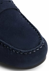 Mocassino in camoscio blu navy con cuciture a contrasto, punta rotonda e superficie testurizzata, dotato di una suola piatta e flessibile per il massimo comfort.