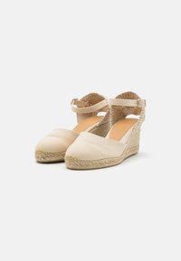 Beige espadrille wedge shoes with canvas upper, braided jute sole, ankle strap fastening, and textured back panel.