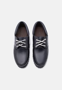 Μαύρα δερμάτινα παπούτσια με λευκά κορδόνια, στρογγυλερή μύτη και διακοσμητικές ραφές γύρω από την άκρη. Η σόλα έχει υφή για καλύτερη πρόσφυση.