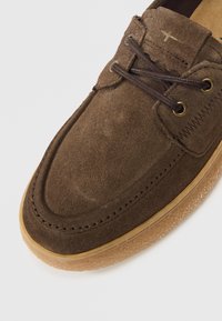 Καφέ σουέτ παπούτσι με στρογγυλεμένη μύτη, με σκούρα καφέ κορδόνια, χρυσούς κρίκους και σόλα από υφή καουτσούκ σε χρώμα τσίχλας.