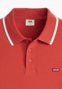 Crvena polo majica od teksturirane pamuka, s dvostrukim gumbom, rebrastim ovratnikom s bijelim rubom i malim Levi's logotipom na prsima.