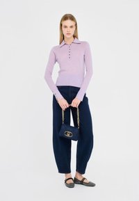 Polo a maniche lunghe lavanda con bottoni, abbinato a jeans larghi blu scuri e una piccola borsa a tracolla trapuntata blu navy con dettagli dorati.