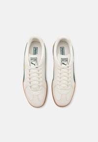 Scarpe sportive bianche in materiali scamosciati e in pelle, con accenti verdi e gialli, chiusura con lacci e suole in gomma.
