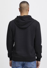 Sudadera con capucha negra de corte ajustado en la parte inferior y en los puños, con una gran capucha y una textura de tela suave. Combinada con unos jeans de mezclilla azules.