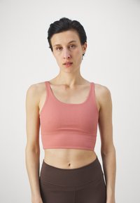 Ριχτό τοπ σε απαλό ροζ ύφασμα με λεπτές τιράντες, συνδυασμένο με καφέ κολάν ψηλόμεσα, με λείο υφή και εφαρμοστό σχέδιο.