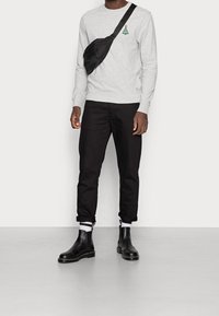 Felpa grigia con grafica di un albero verde, borsa nera a tracolla, jeans neri arrotolati e stivaletti Chelsea neri con suole texturizzate.