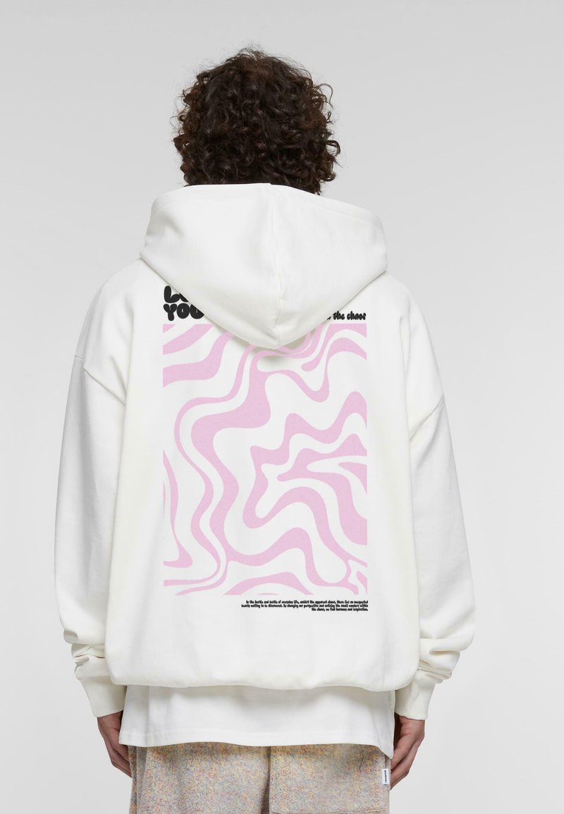 Felpa bianca con cappuccio caratterizzata da un motivo ondulato rosa sulla schiena, con testo nero sopra e sotto il design. Tessuto morbido, vestibilità comoda.