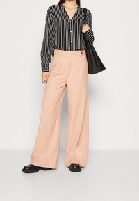 Černobílý pruhovaný košile s knoflíky, spárovaná s kalhotami s vysokým pasem a širokými nohavicemi v světle růžové barvě. Černá taška a masivní černé boty dokončují vzhled.