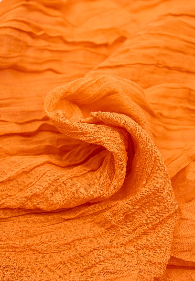 Teksturowana, pomarszczona pomarańczowa tkanina. Lekki, przezroczysty materiał o miękkich fałdach i lekko luźnym splocie, co tworzy płynny wygląd.