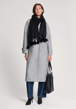 Cappotto di lana grigio con taglio dritto, sciarpa nera con dettagli a pom-pom e stivali neri con tacco alto; abbinato a una borsa nera.