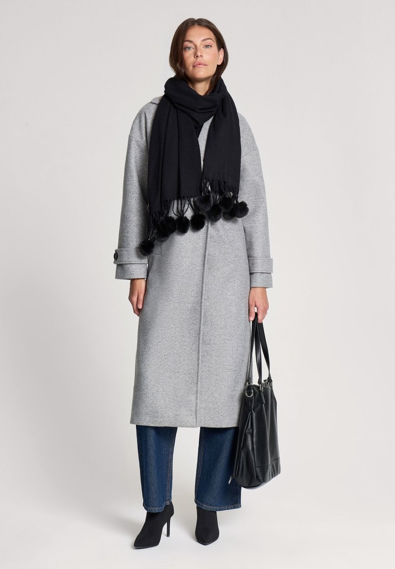 Szary wełniany płaszcz o prostym kroju, czarny szal z pomponami i czarne kozaki na wysokim obcasie; w zestawie z czarną torebką.