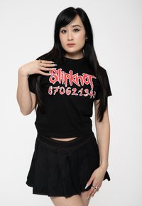 Black cropped t-shirt with red "Slipknot" logo and numbers. Paired with a black pleated mini skirt, featuring contrasting stitching.