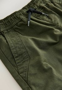 Olivové bavlnené kraťasy s elastickým pásom, čierne šnúrky a bočná vrecko; hladká textúra a čisté švíky.