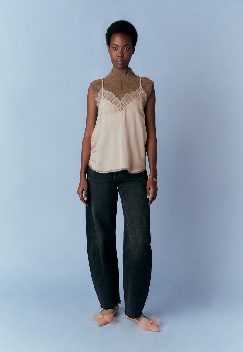 Ärmlös beige satinblus med spetsdetaljer, kombinert med högmidjade mörka denimjeans och ljusrosa mules med tyllaccent.