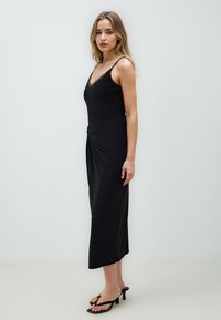 Zwarte mouwloze jurk met een V-halslijn, versierd met kantafwerking, een gedraaide voorkant en een vloeiende, enkel-lange silhoët.