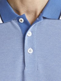 Ljusblå pikétröja med ett strukturerat mönster, tre vita knappar och en krage med en mörkare blå accent.