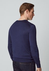 Marineblaue Strickjacke mit langen Ärmeln, rundem Ausschnitt und strukturierten Ellenbogenpatches. Glattes Material mit tailliertem Schnitt.