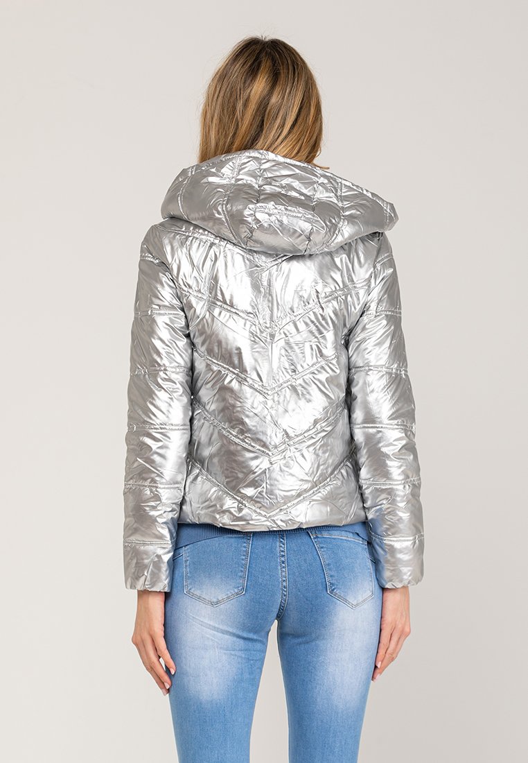 Giacca a vento argento con cappuccio, caratterizzata da un design trapuntato, finitura testurizzata e silhouette aderente. Indossata con jeans blu.