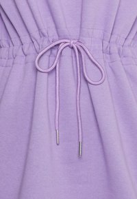 Tissu de sweat-shirt violet présentant une ceinture élastique avec un cordon de serrage noué, fini avec deux embouts métalliques. Texture lisse sur l'ensemble.