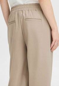 Pantalons beiges avec une taille élastique, des poches arrière avec des détails plats et un tissu lisse et texturé.