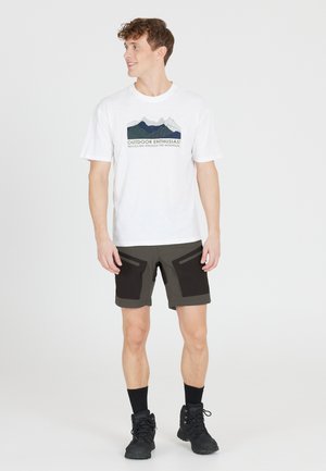 Herren T-Shirt aus weißer Baumwolle mit Berggrafik und Text, kombiniert mit dunkelgrünen Shorts mit schwarzen Akzenten und Taschen, getragen mit schwarzen Stiefeln.