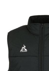 Gilet imbottito nero con colletto alto, chiusura con zip e logo ricamato sul lato sinistro. Il tessuto ha una texture liscia e morbida.