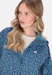 Blå leopardmönstrad jacka med ljusblå krage, dragkedja och en liten logotyp framtill. Slätt, lätt material.