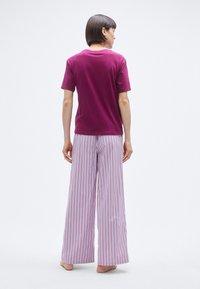 T-shirt en coton violet à manches courtes, associé à un pantalon large à fines rayures violet clair. Texture lisse et coupe décontractée.