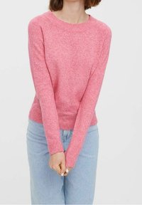 Pink knitted sweater with a round neckline and ribbed cuffs. It has a textured finish and is paired with light blue high-waisted jeans.