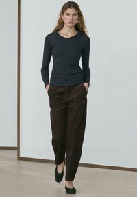 Haut à manches longues bleu marine avec un col rond, associé à un pantalon en velours côtelé marron. Les chaussures sont noires, sans lacets, avec une texture plissée.