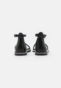 Black leather sandals with a back strap, featuring a braided design and a contrasting white stitching around the sole.