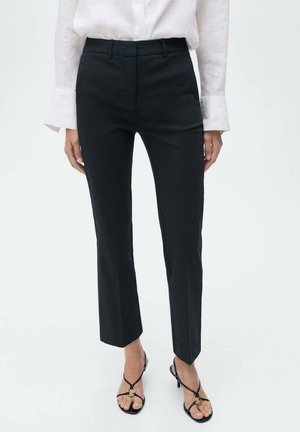 Pantalons noirs ajustés à coupe droite, avec une taille mi-haute, des passants de ceinture et une texture de tissu lisse. Associés à des sandales noires à lanières.