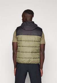 Gilet rembourré avec des blocs de couleurs vert et noir, doté d'une capuche ajustée et d'une texture matelassée horizontale. Design léger et décontracté.