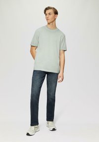 Lichtgrijs T-shirt met korte mouwen en ronde hals, gedragen met donkerblauwe rechttoe-rechtaan jeans en beige sneakers met grijze accenten.