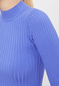 Top de punto acanalado de cuello alto en azul claro. Presenta un diseño ajustado con un cuello alto y una superficie texturizada.